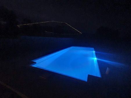 A Modern House With A Swimming Pool In The Backyard At Night — Pool Builder in Moore Creek, NSW