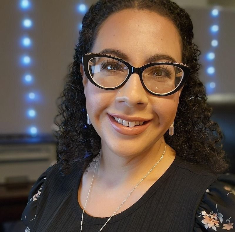 A woman wearing glasses and a necklace smiles for the camera