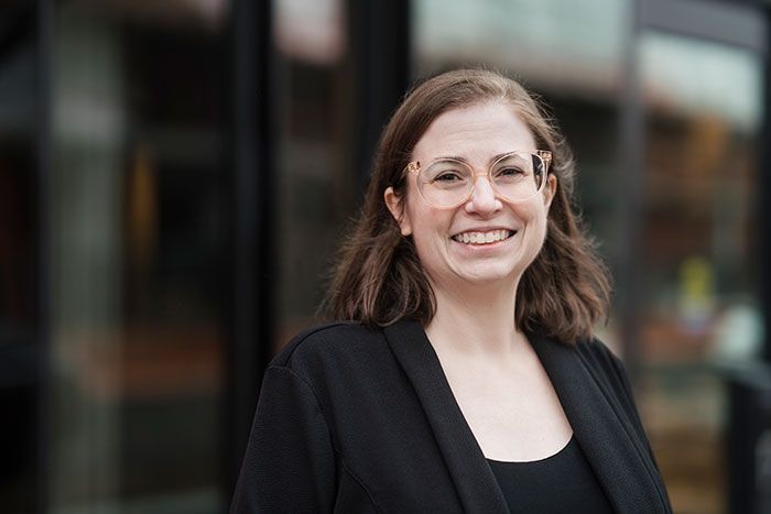 A woman wearing glasses and a black jacket is smiling for the camera.