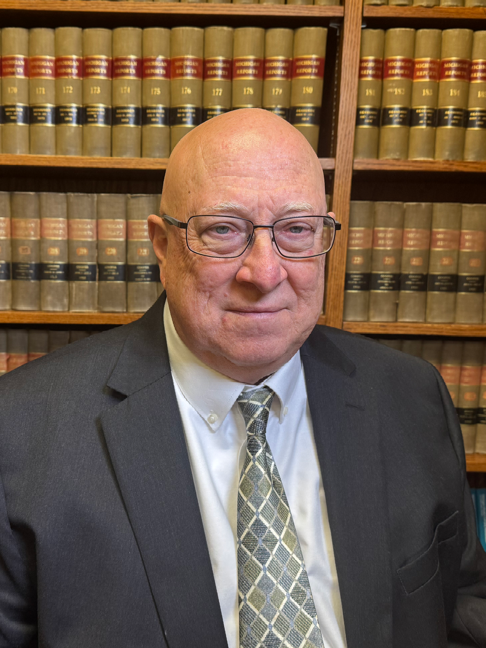 A man in a suit and tie is standing in front of a bookshelf.
