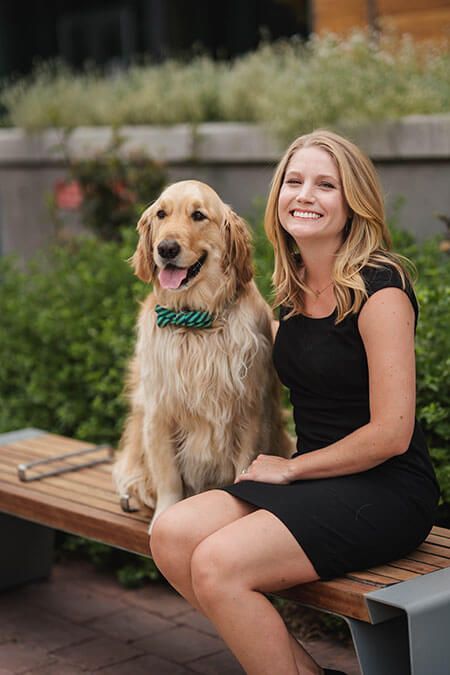 A woman is sitting on a bench next to a dog.