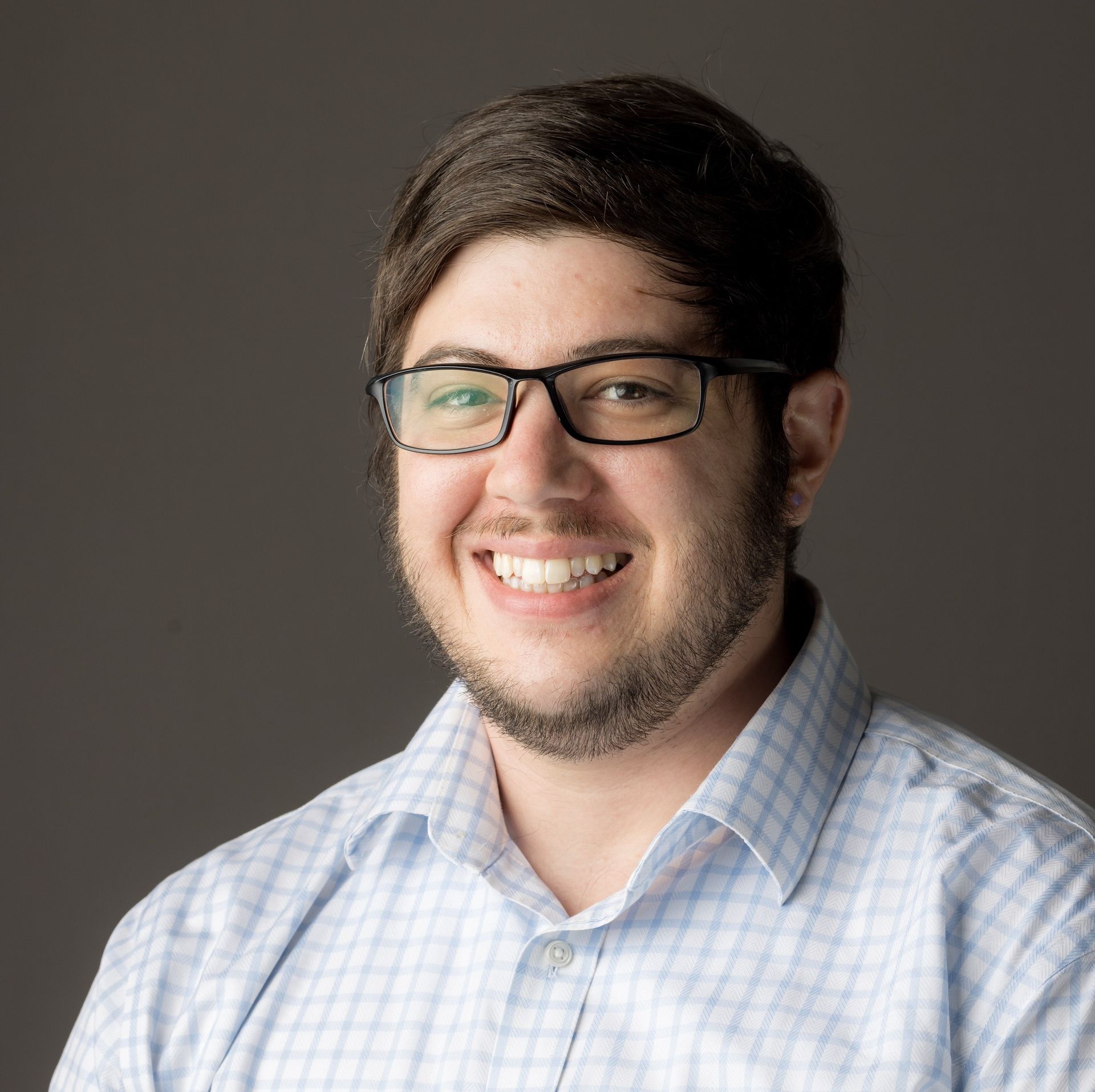 A man wearing glasses and a plaid shirt is smiling for the camera.