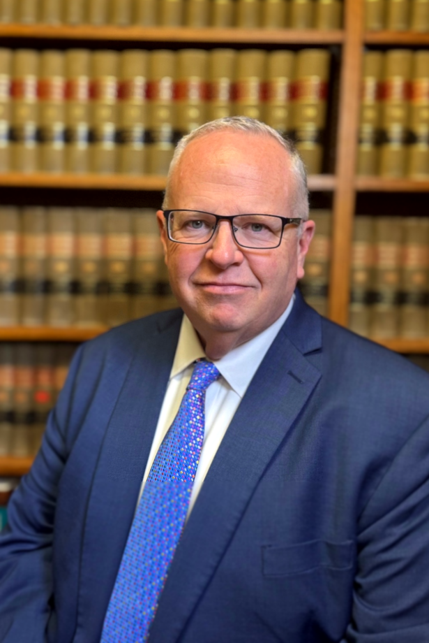 A man in a suit and tie is standing in front of a bookshelf.