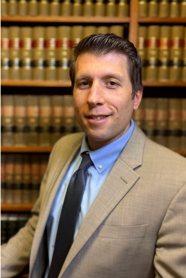 A man in a suit and tie is standing in front of a bookshelf.