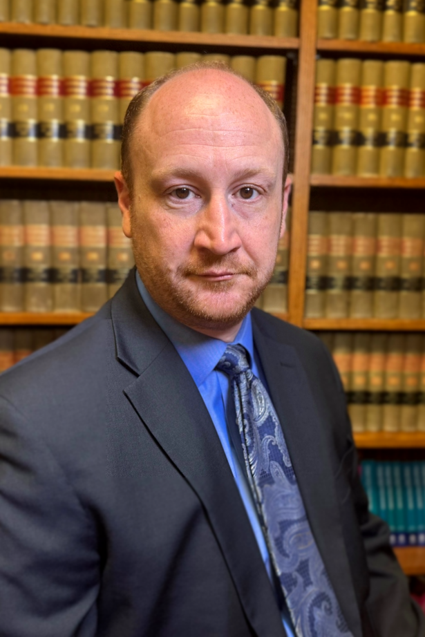 A man in a suit and tie is standing in front of a bookshelf.