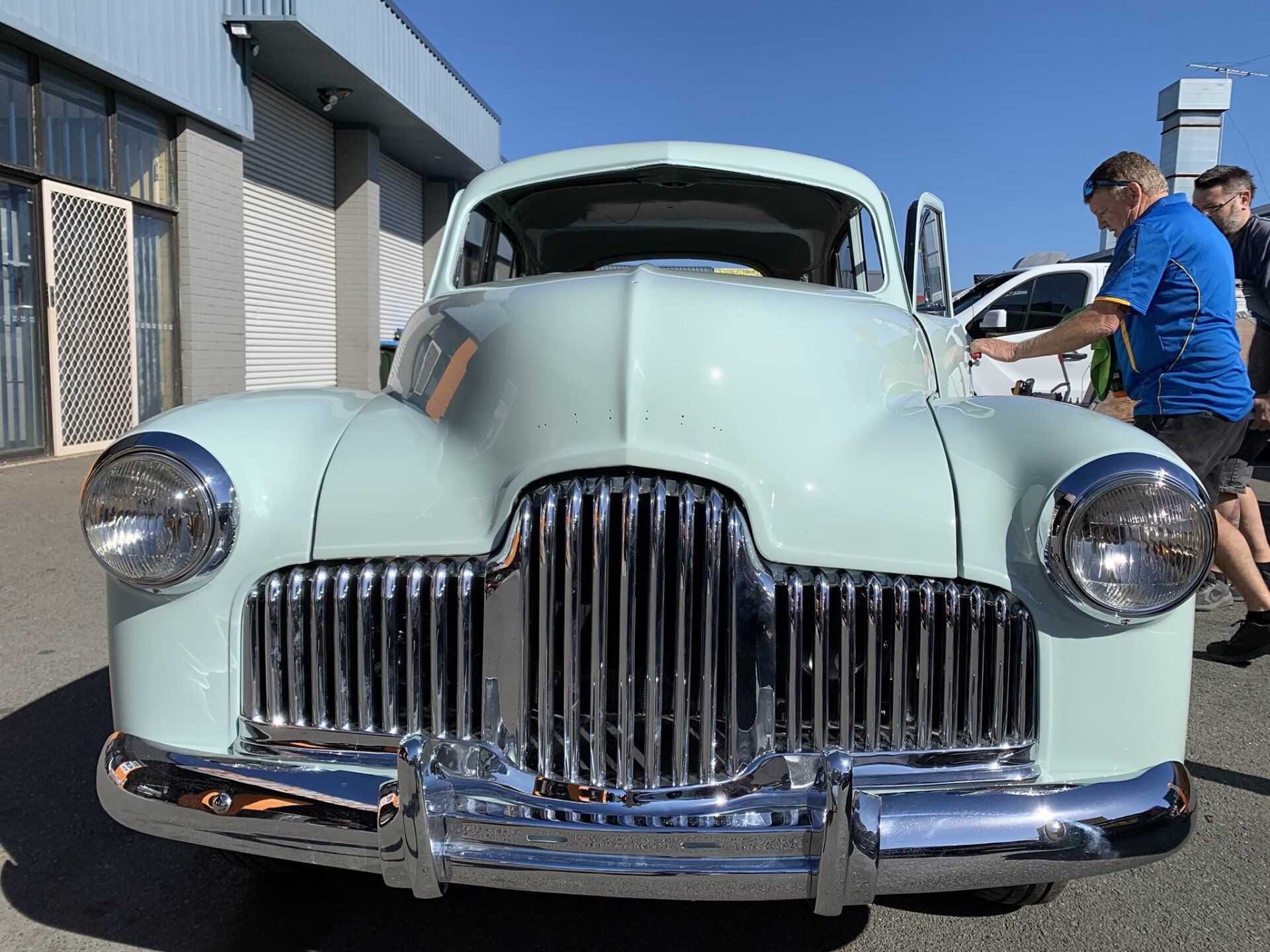 A man in a blue shirt is standing next to an old car.