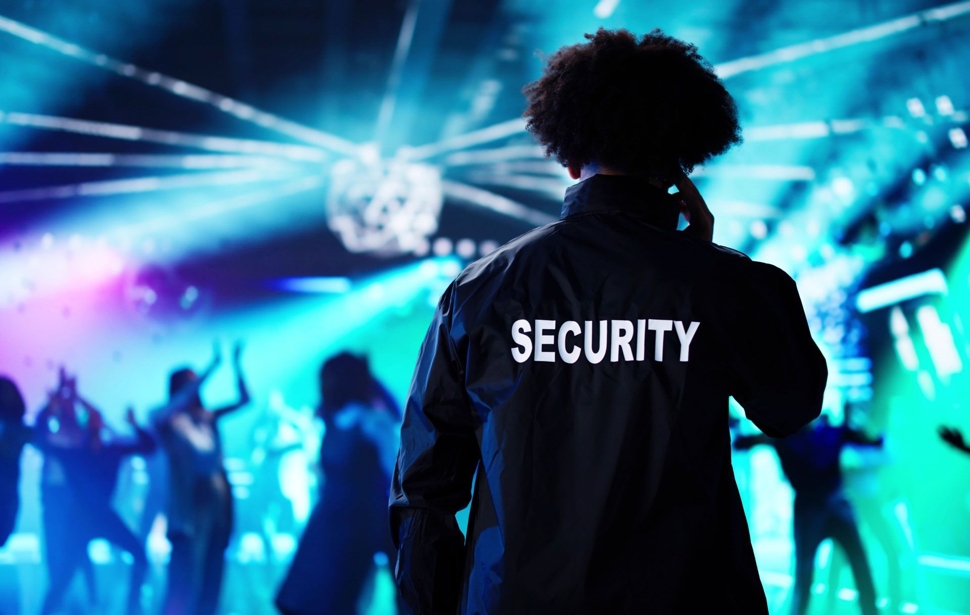 Security guard at a nightclub, watching dancers under colorful lights.