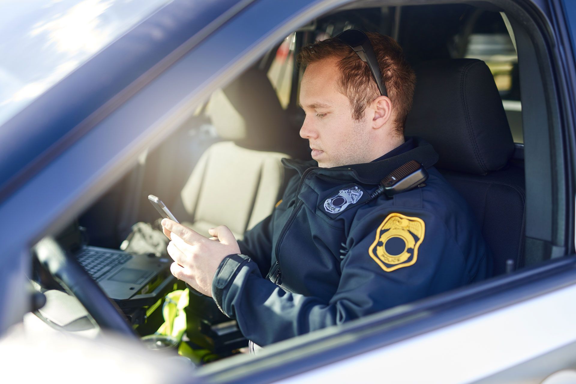 Police officer in uniform using a phone inside a patrol car.
