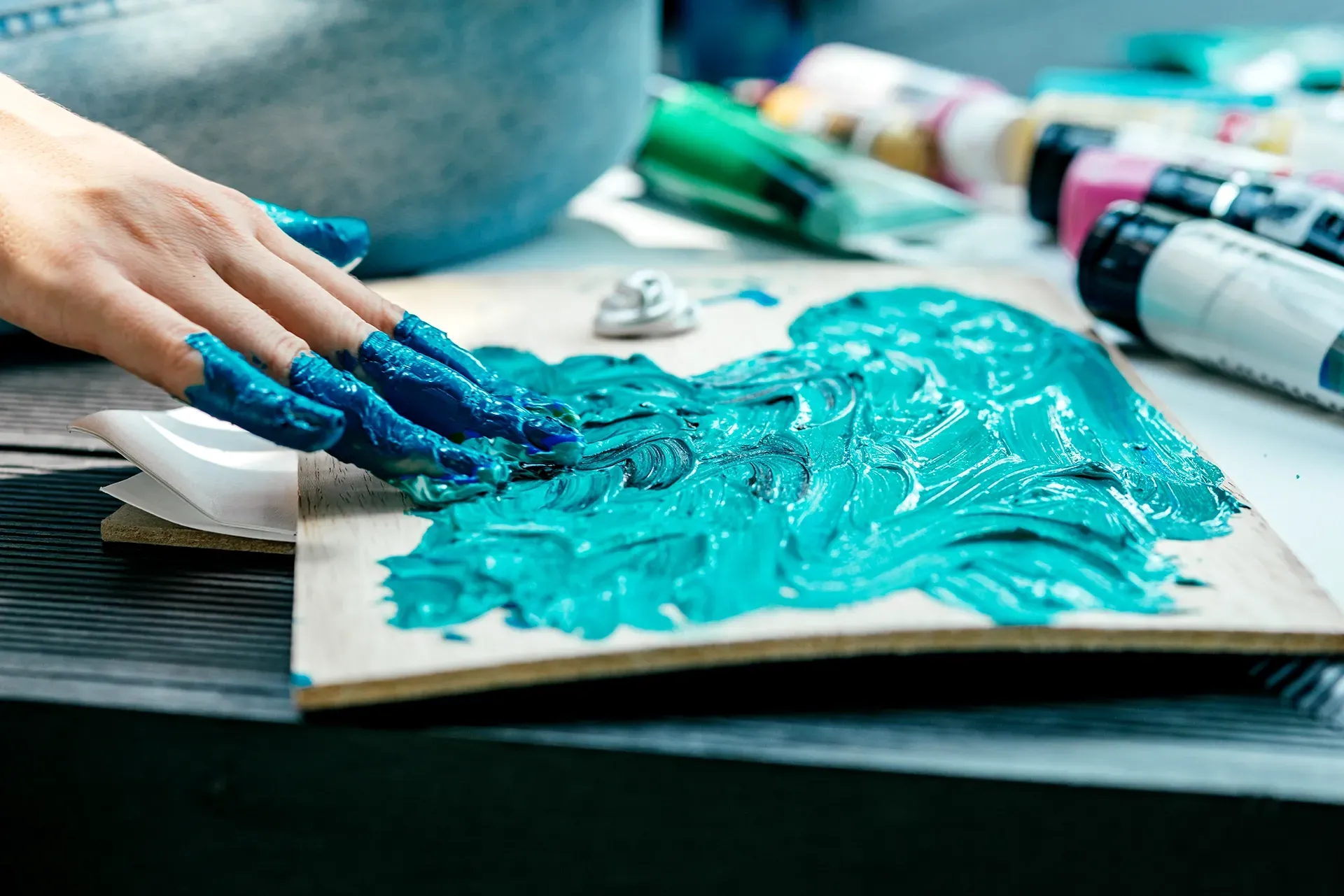 Eine Person trägt mit den Händen blaue Acrylfarbe auf ein Stück Holz auf.