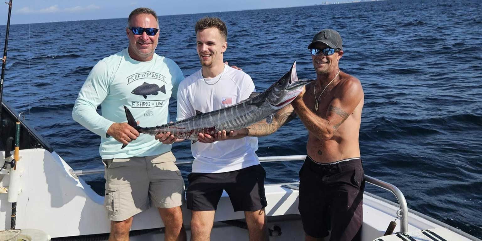 Three men are standing on a boat holding a large fish.