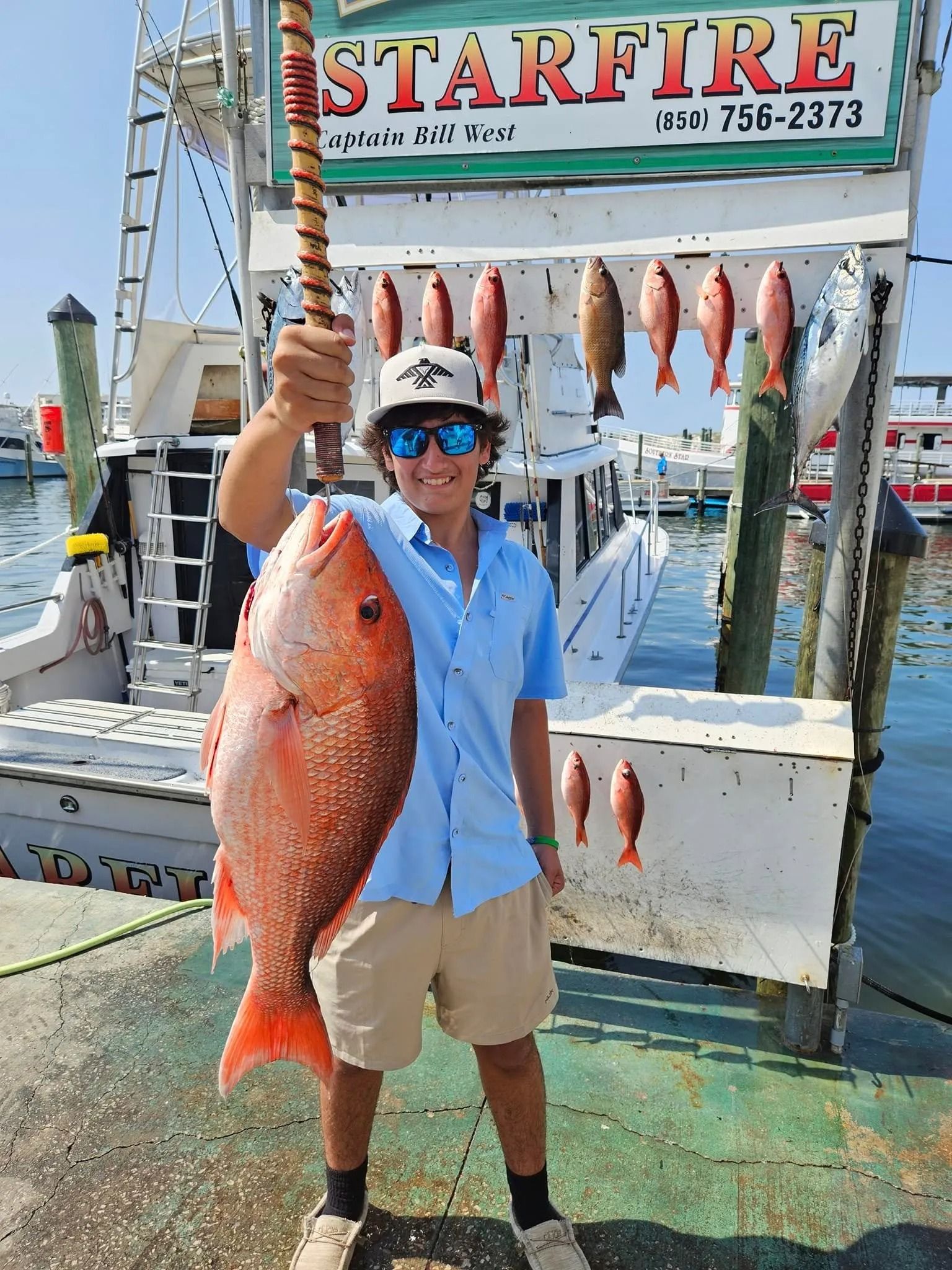 A man is holding a large red fish in front of a sign that says starfire