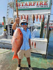 A man is holding a large red fish in front of a sign that says starfire
