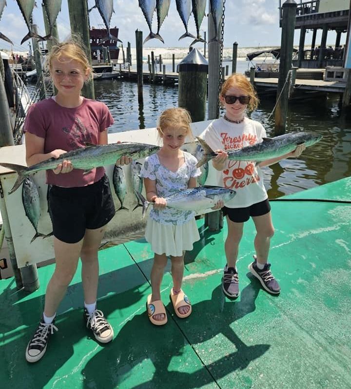 Three young girls holding fish in front of a dock that says freshly caught