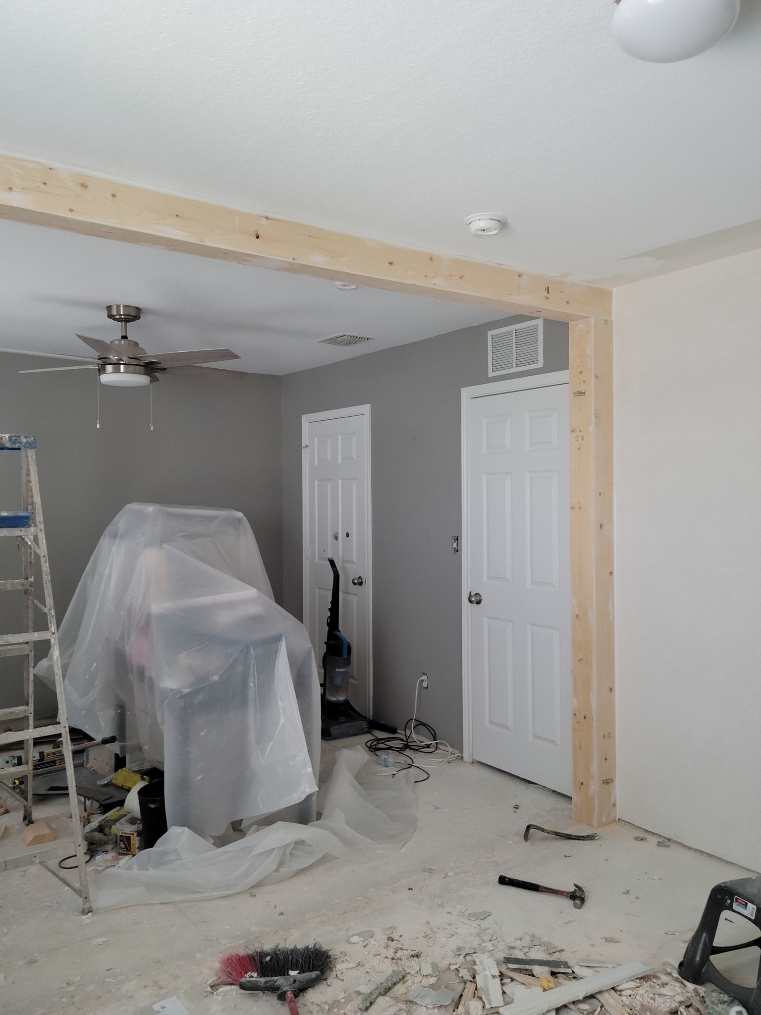 A living room is being remodeled with a ceiling fan and a wooden beam.