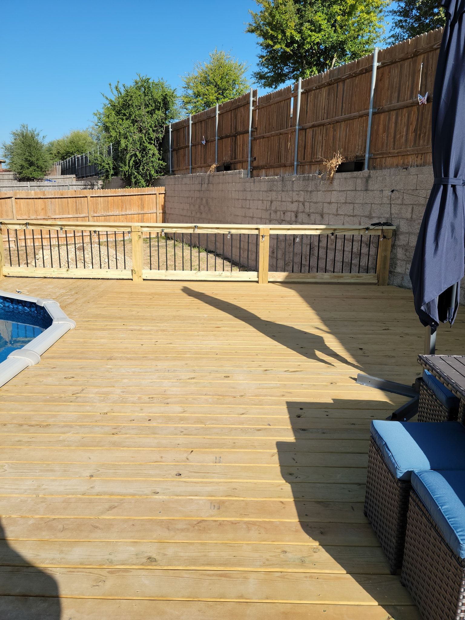 A wooden deck with a fence and a pool in the background.