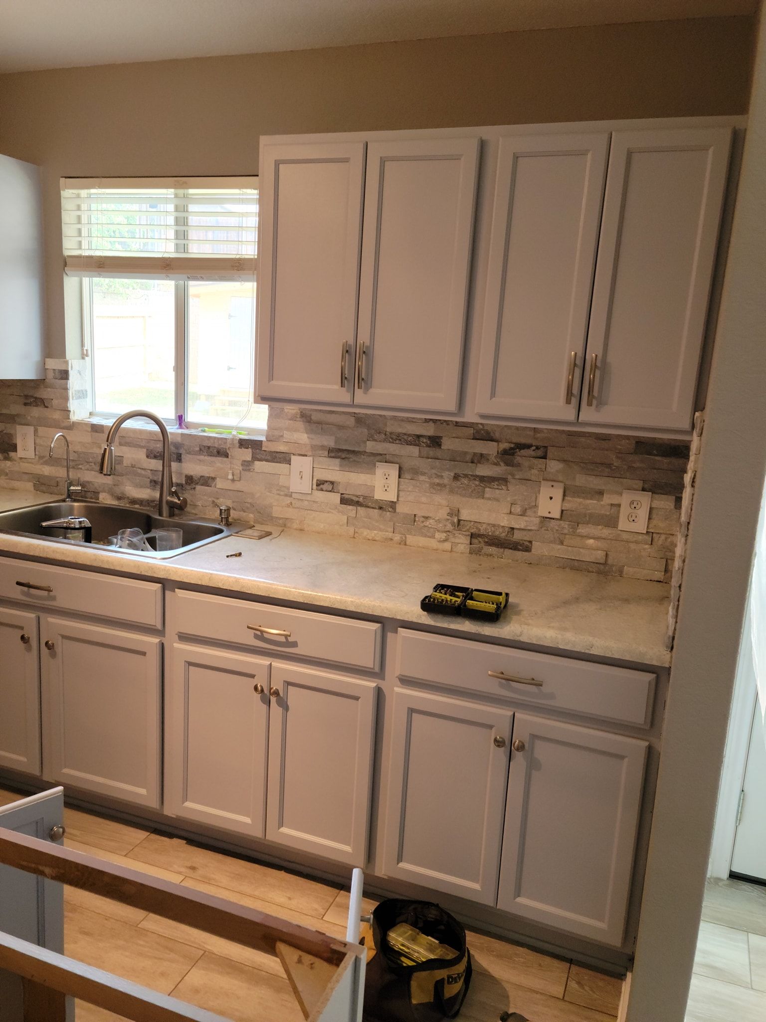 A kitchen with white cabinets , a sink , and a window.