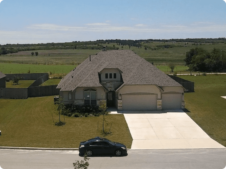 A black car is parked in front of a large house