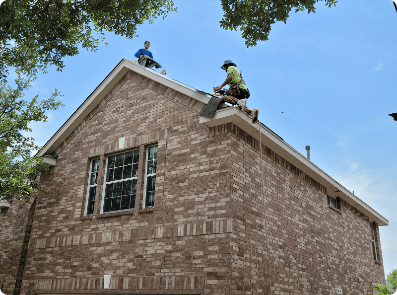 Two men are working on the roof of a brick house.