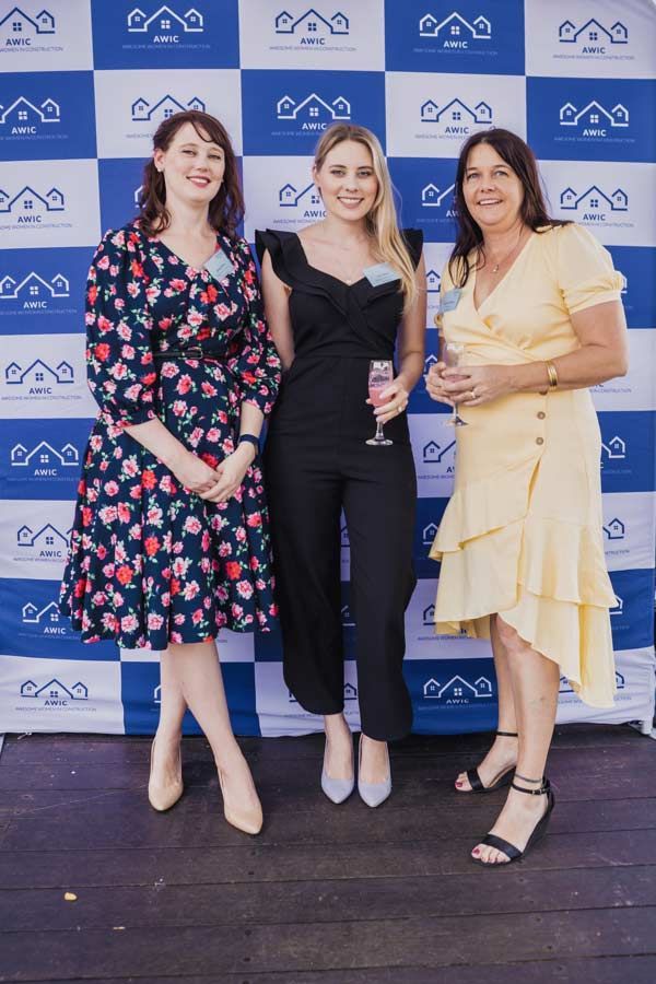 Three Women Are Posing For A Picture In A Blue And White Checkered Backdrop — Nyblad Construction in Caloundra West, QLD