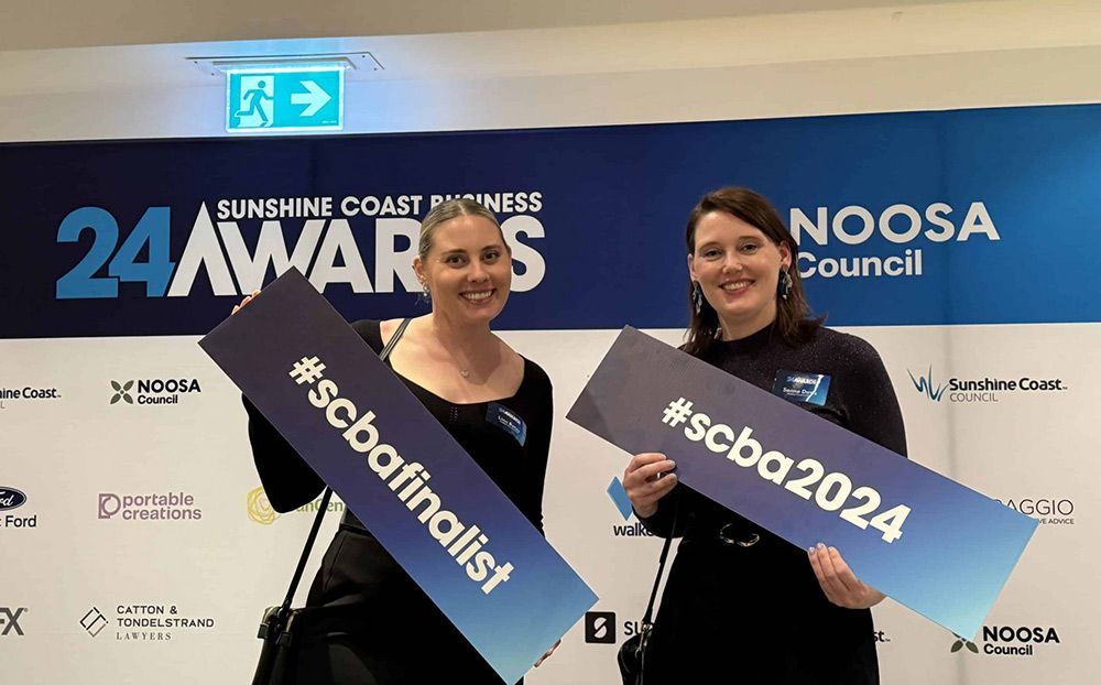 Two Women Are Holding Signs In Front Of A Noosa Council Banner — Nyblad Construction in Caloundra West, QLD