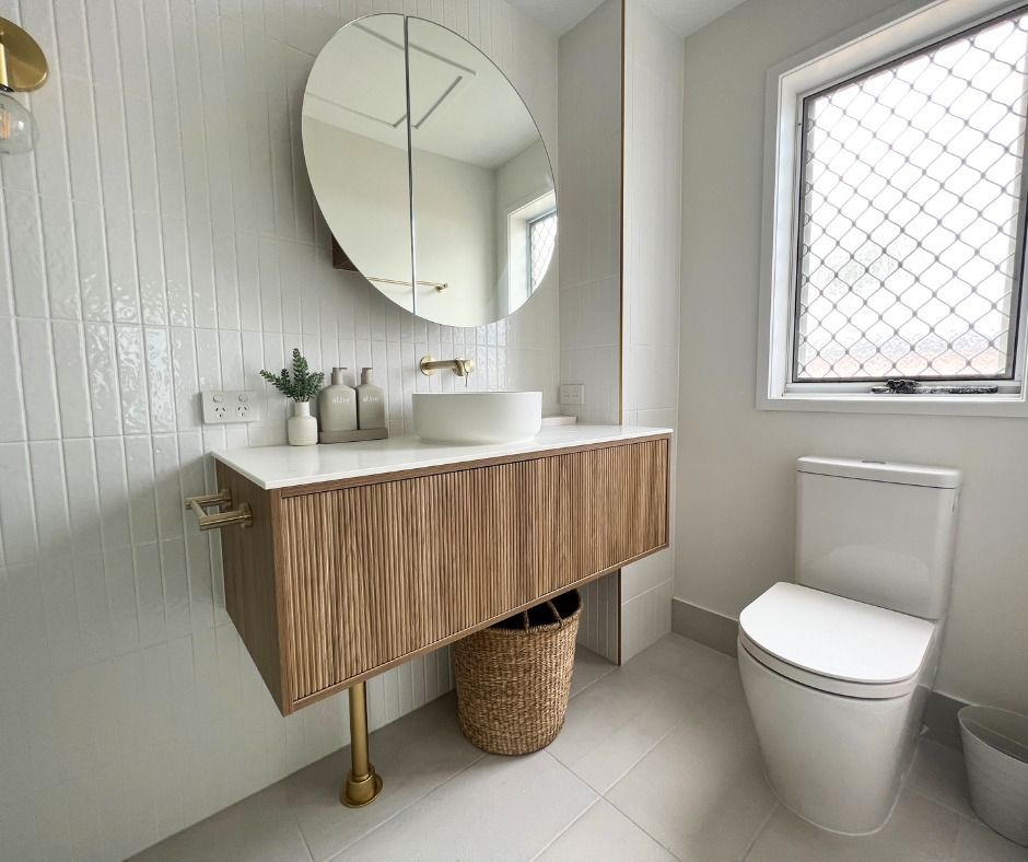 A Modern Bathroom With a Wooden Vanity, Round Mirror, and White Tiles — Nyblad Construction in Coolum, QLD