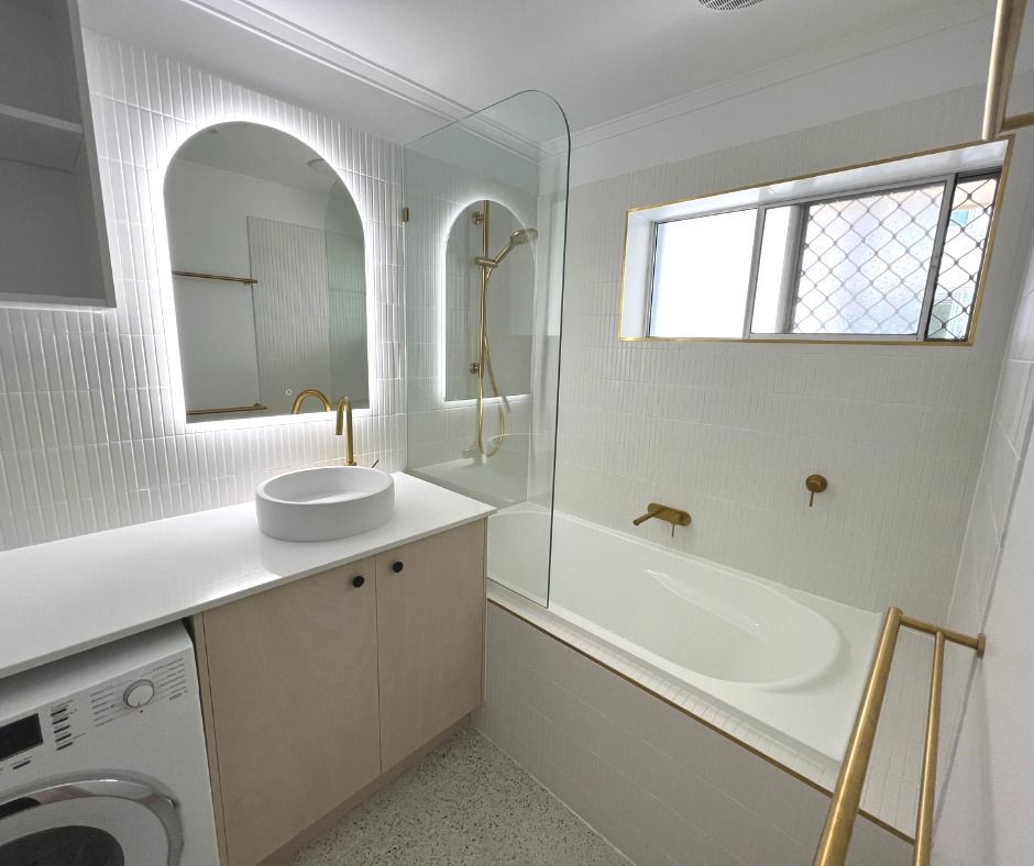 Modern White Bathroom With an Arched Mirror, a Bathtub, and Gold Fixtures — Nyblad Construction in Coolum, QLD