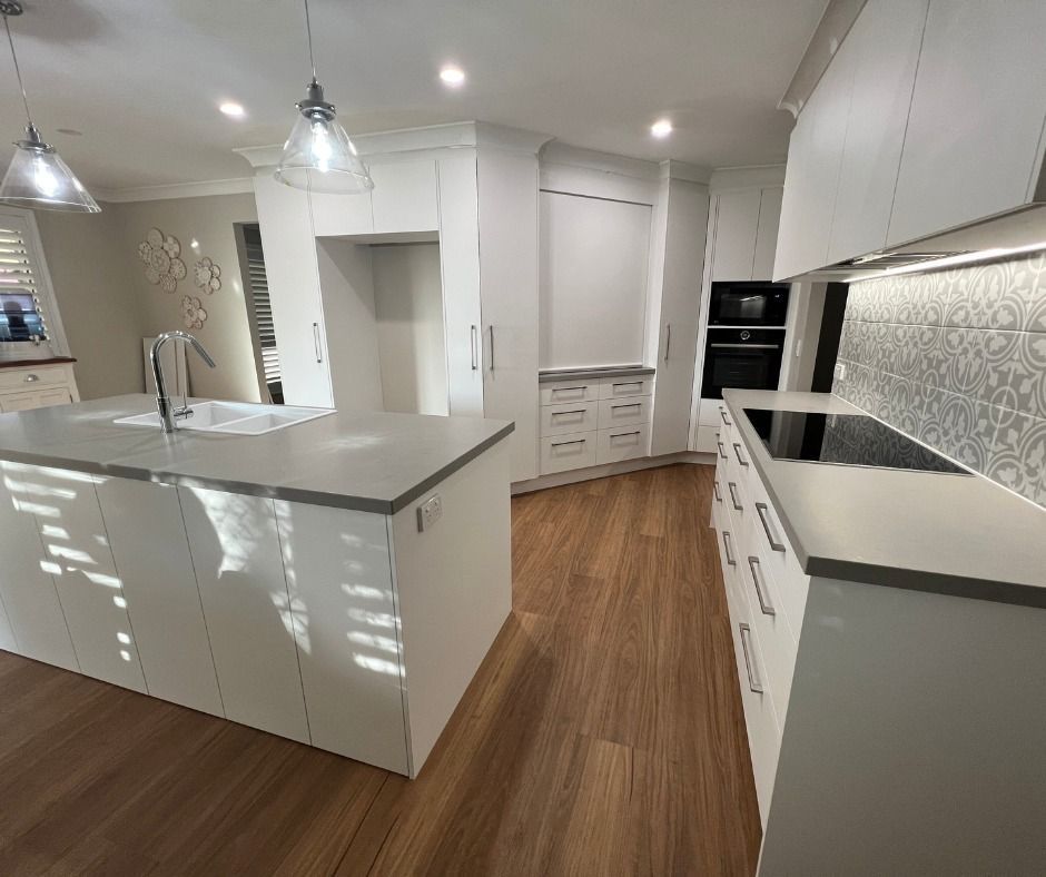 Modern White Kitchen With Island and Integrated Appliances, Light Wood Floors — Nyblad Construction in Caloundra West, QLD