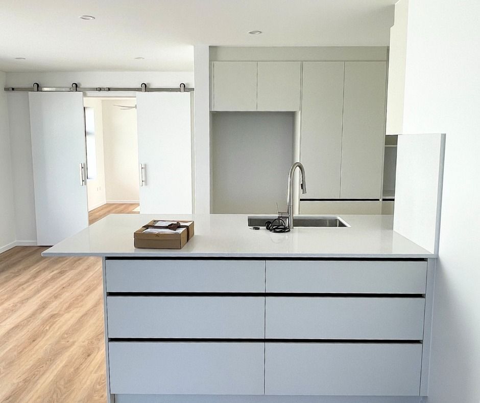 Modern White Kitchen With an Island, Stainless Steel Hardware, and Light Wood Flooring — Nyblad Construction in Maroochydore, QLD