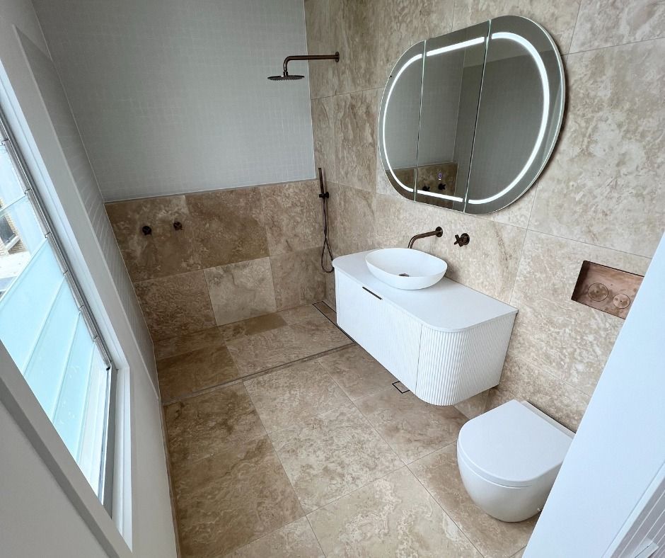 Bathroom With Travertine Tiles, White Vanity, Oval Mirror, and Toilet — Nyblad Construction in Caloundra, QLD
