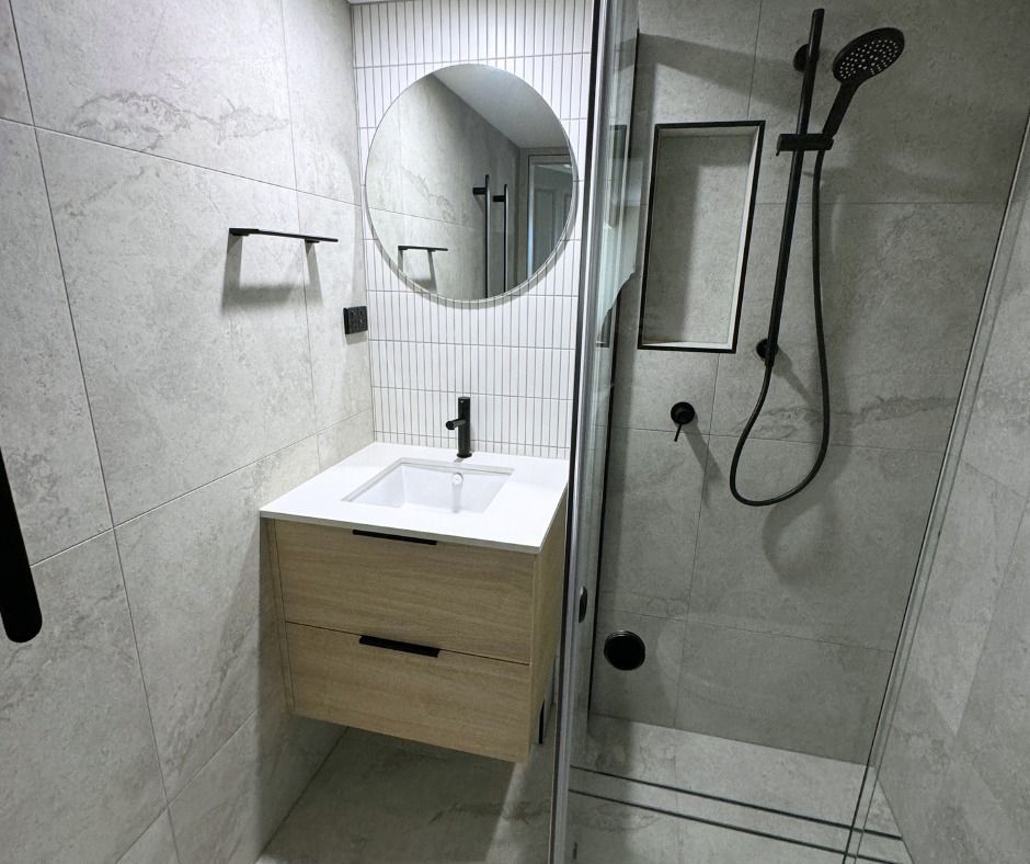 Modern Bathroom With a Wood Vanity, Round Mirror, and Black Fixtures — Nyblad Construction in Coolum, QLD