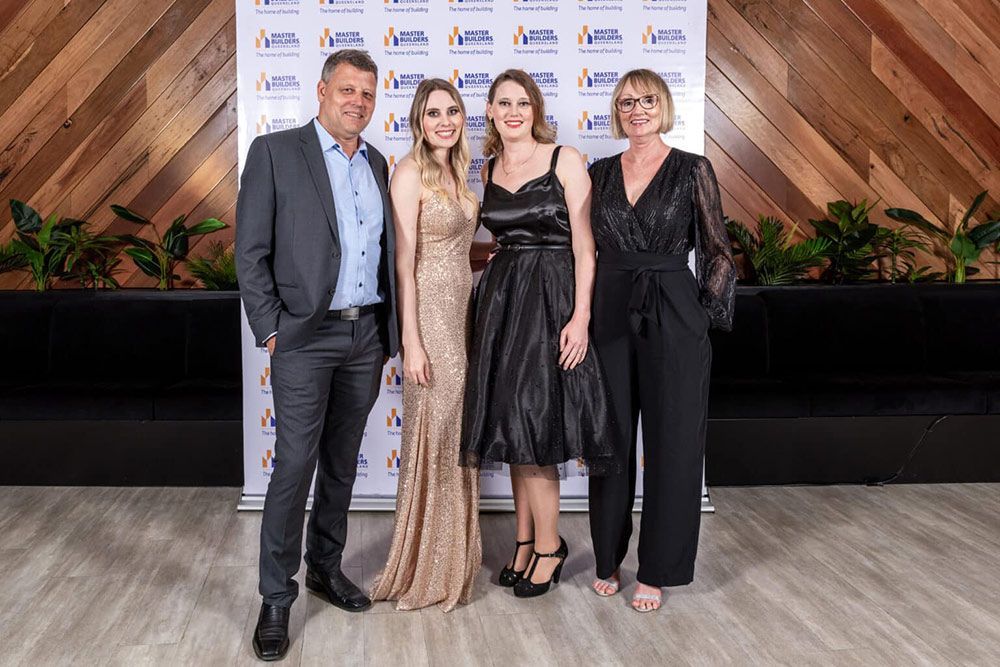 A Group Of People Are Posing For A Picture In Front Of A Wooden Wall — Nyblad Construction in Caloundra West, QLD