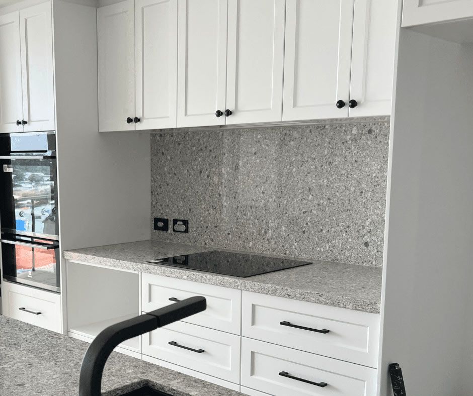 A Kitchen With White Cabinets, Granite Counter Tops, And A Stove Top Oven — Nyblad Construction in Caloundra West, QLD