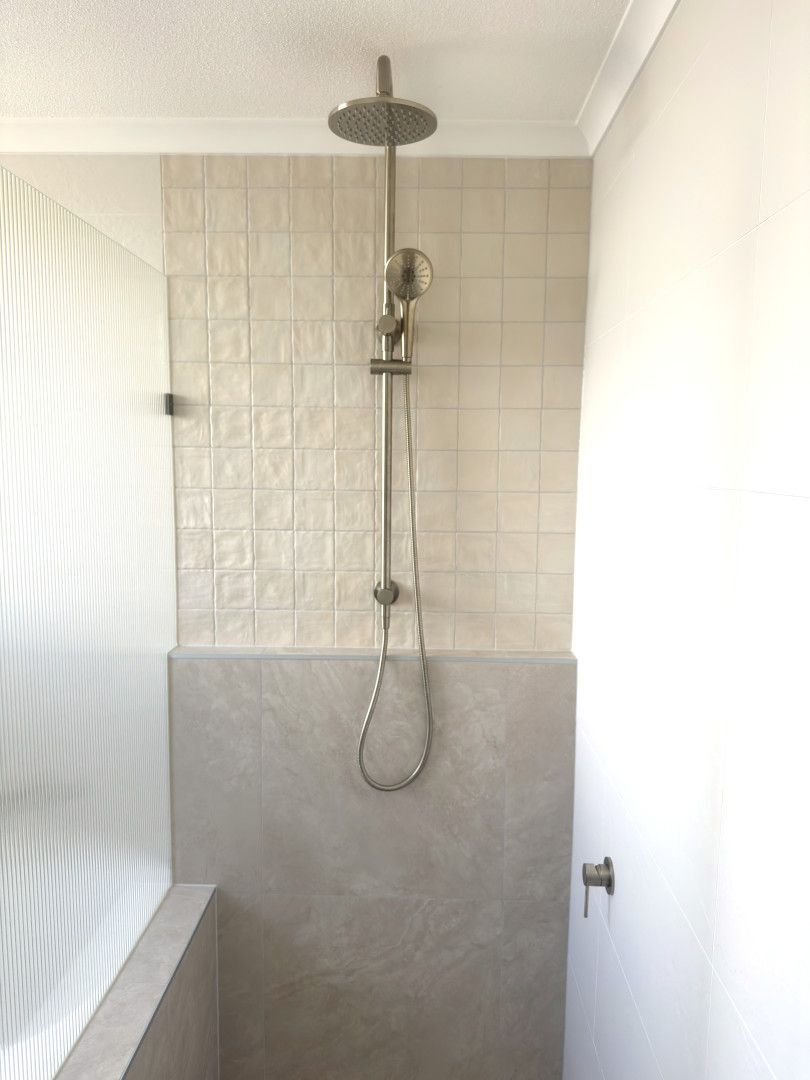 Shower stall with light-colored tile and gray lower panel; showerhead, faucet, and hand shower. — Nyblad Construction in Coolum, QLD