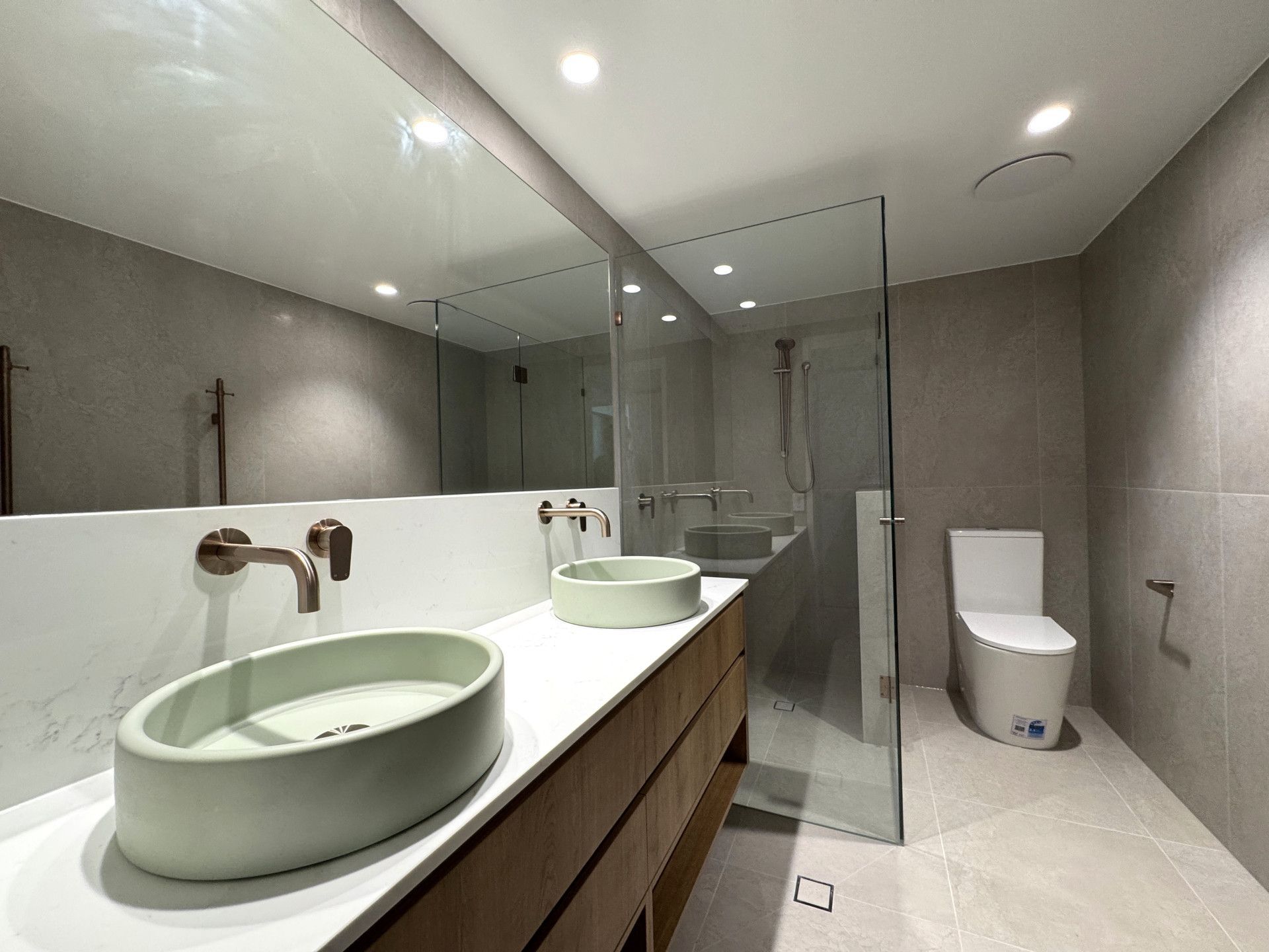 Modern bathroom with two sinks, glass shower, and toilet; gray walls and floor. — Nyblad Construction in Coolum, QLD
