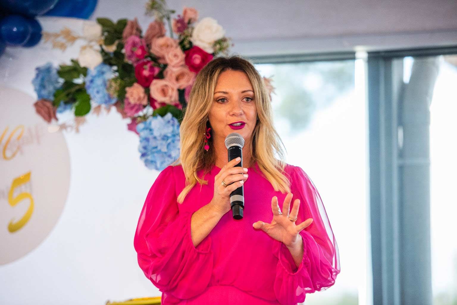 A Woman In A Pink Dress Is Holding A Microphone — Nyblad Construction in Caloundra West, QLD