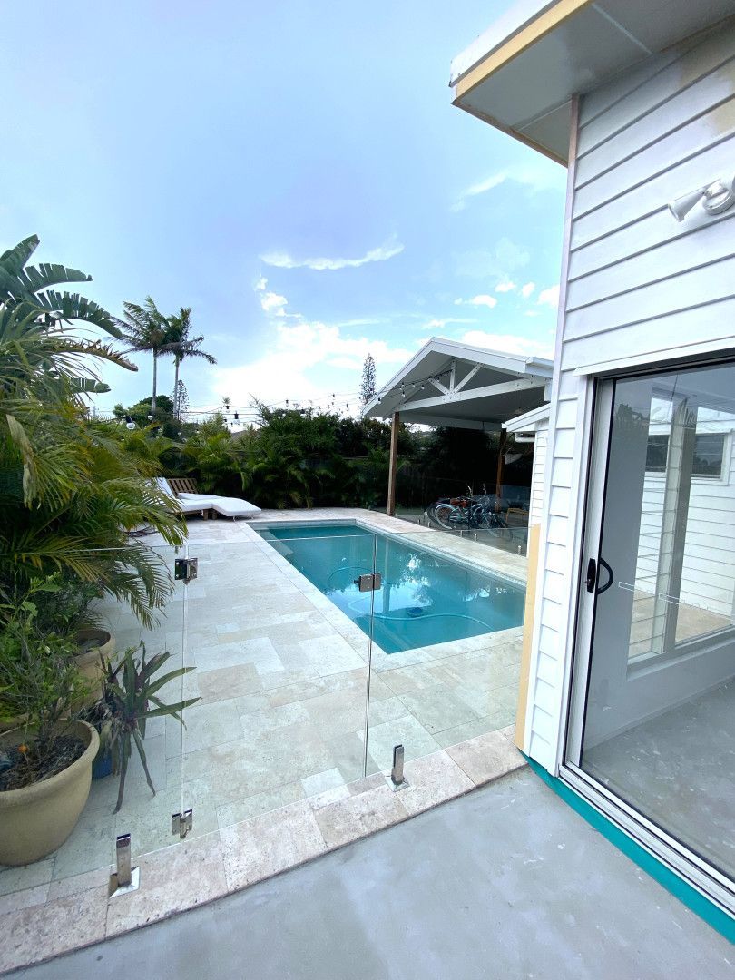Pool with glass fence and white patio, blue water, and covered seating area. — Nyblad Construction in Coolum, QLD