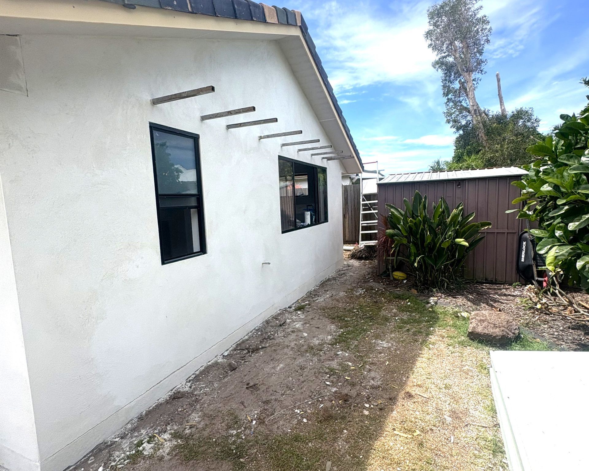 White stucco building with black-framed windows, wood beams, and a small yard. — Nyblad Construction in Coolum, QLD