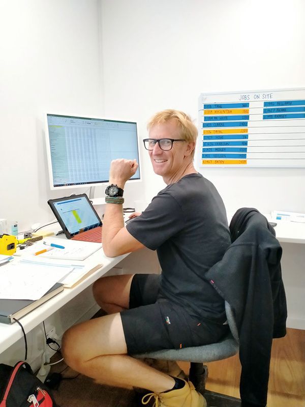 A Man Is Sitting At A Desk In Front Of A Computer — Nyblad Construction in Caloundra West, QLD