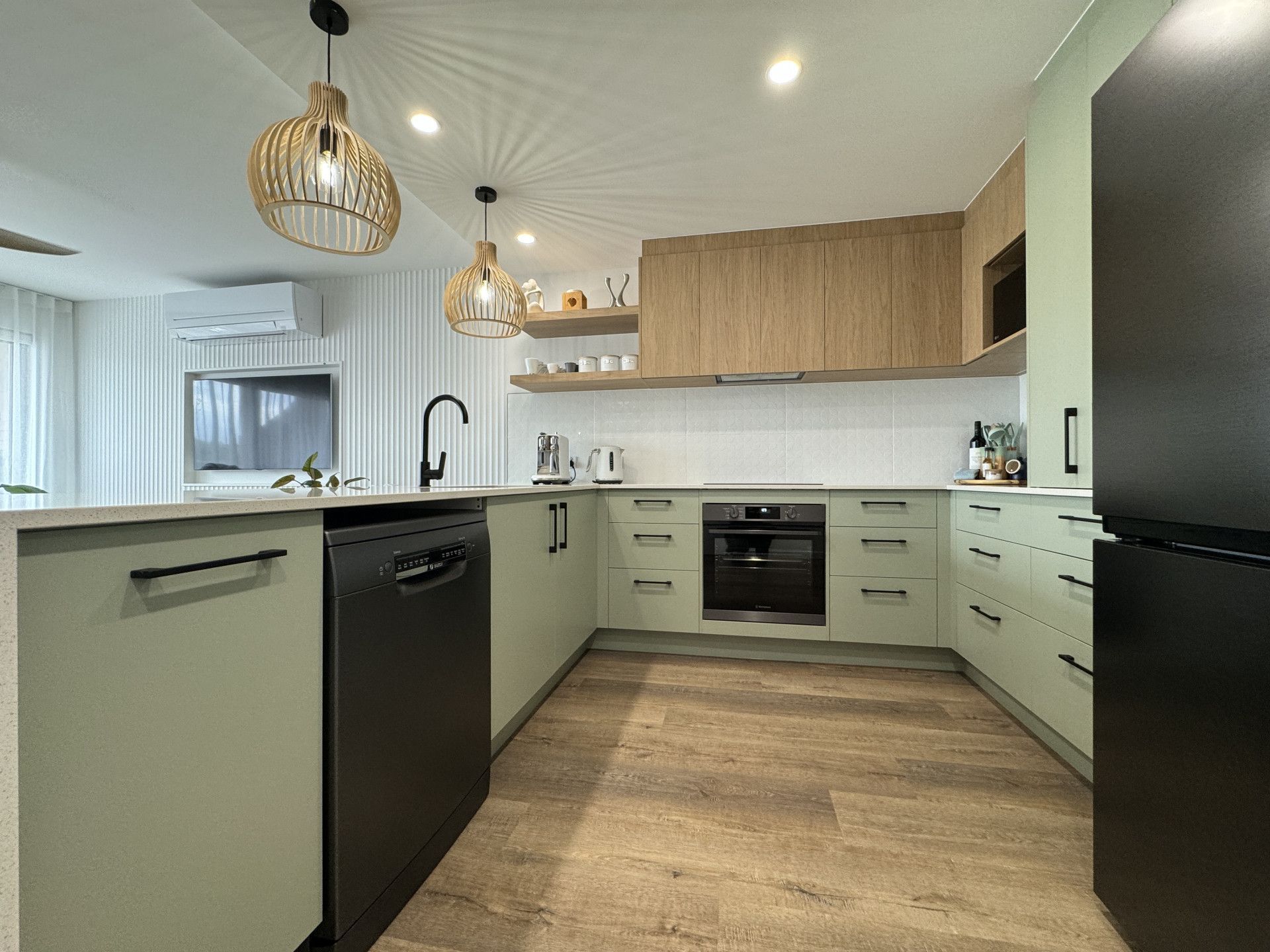 Modern kitchen with light green cabinets, black appliances, and wooden accents.