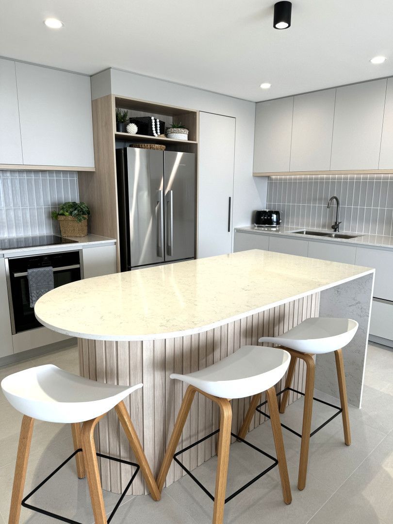 Modern kitchen with an oval island, light wood accents, stainless steel appliances, and white stools.