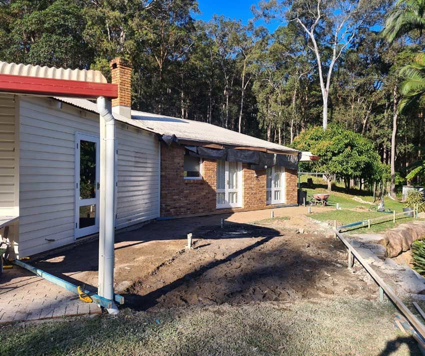 A White House With A Red Roof Is Surrounded By Trees And Dirt — Nyblad Construction in Caloundra West, QLD