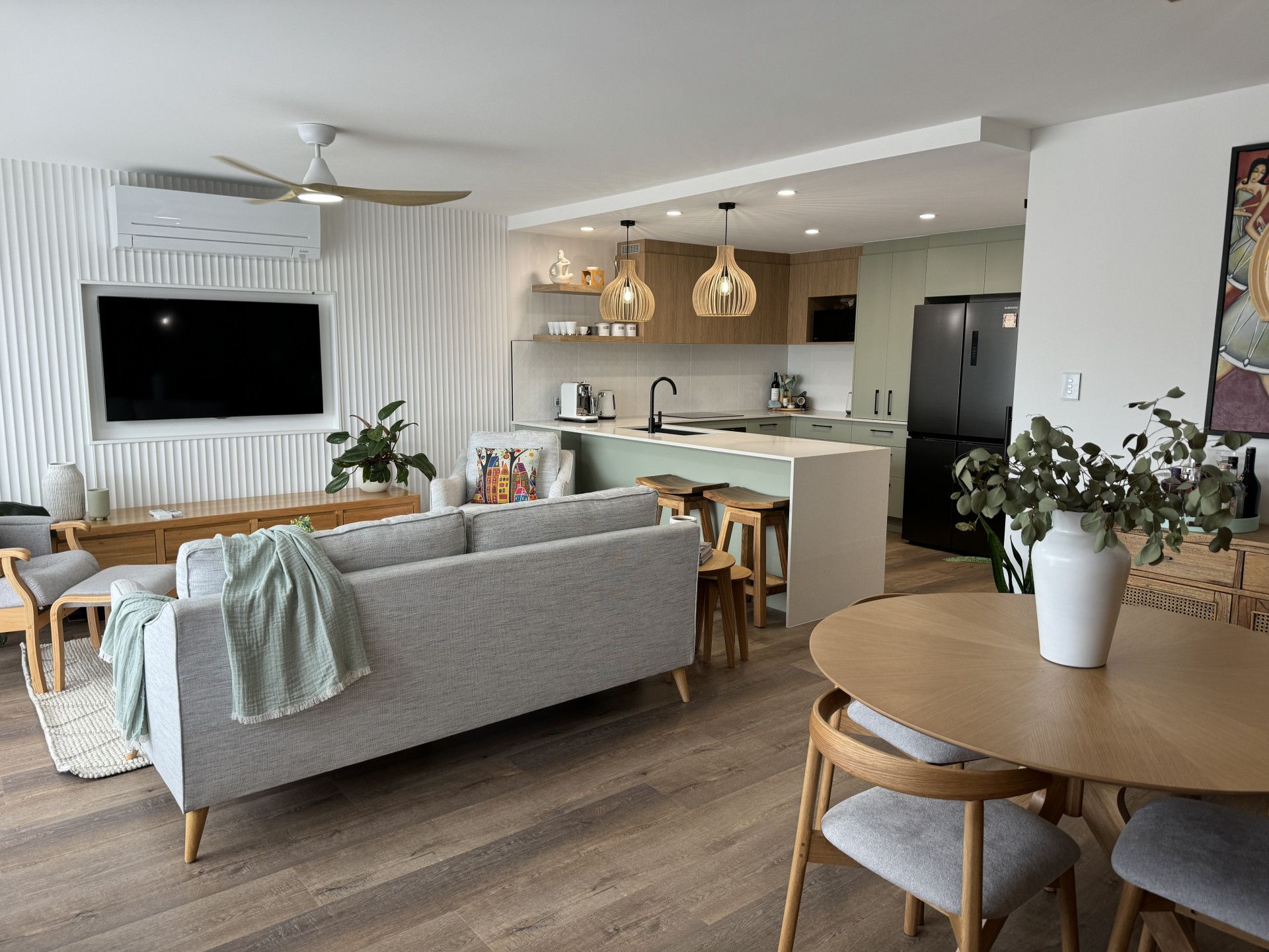 Modern living room with open kitchen. Gray sofa, wooden dining table, and green accents. — Nyblad Construction in Maroochydore, QLD