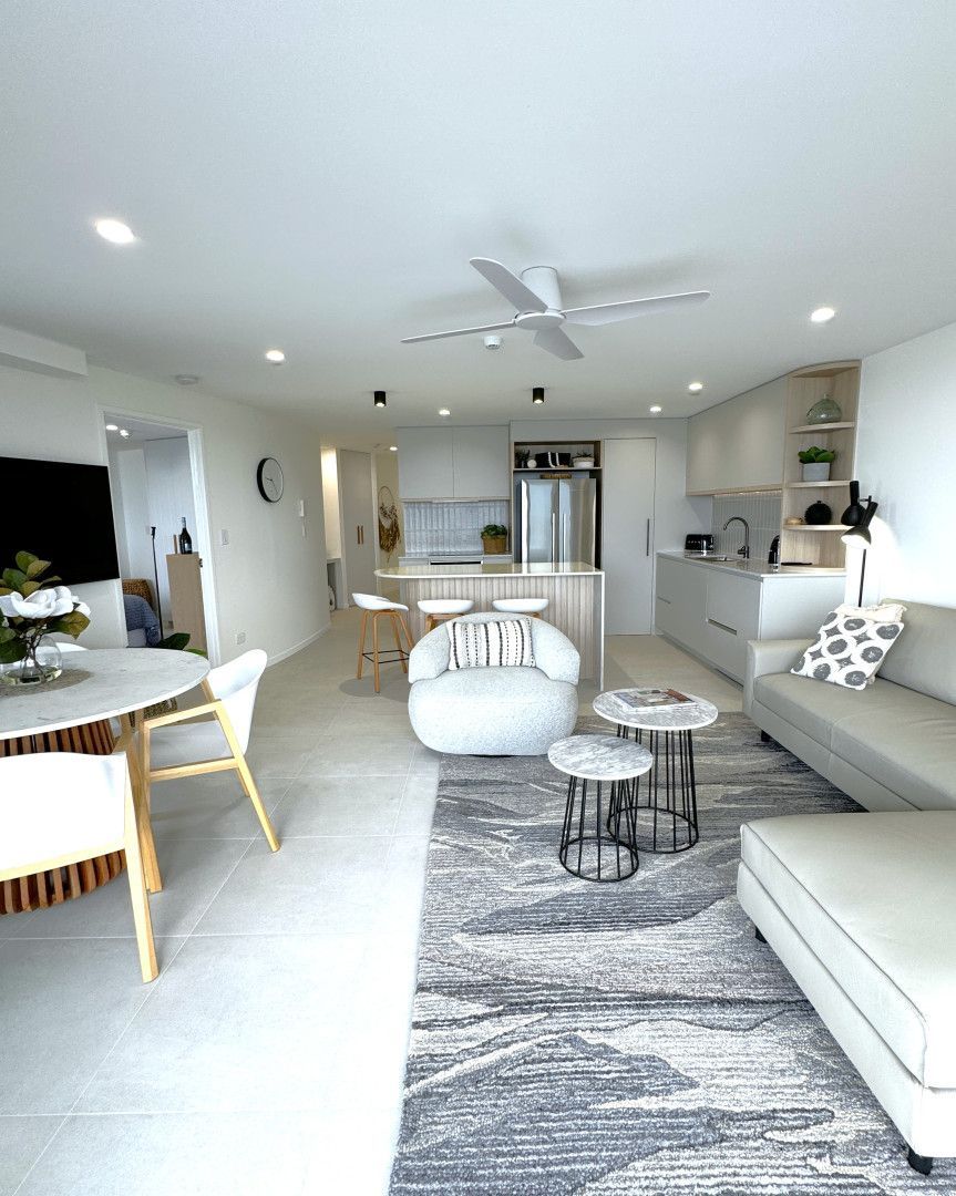 Open-plan living space with kitchen, dining, and living areas. White walls, light wood, neutral furniture, and a rug. — Nyblad Construction in Maroochydore, QLD