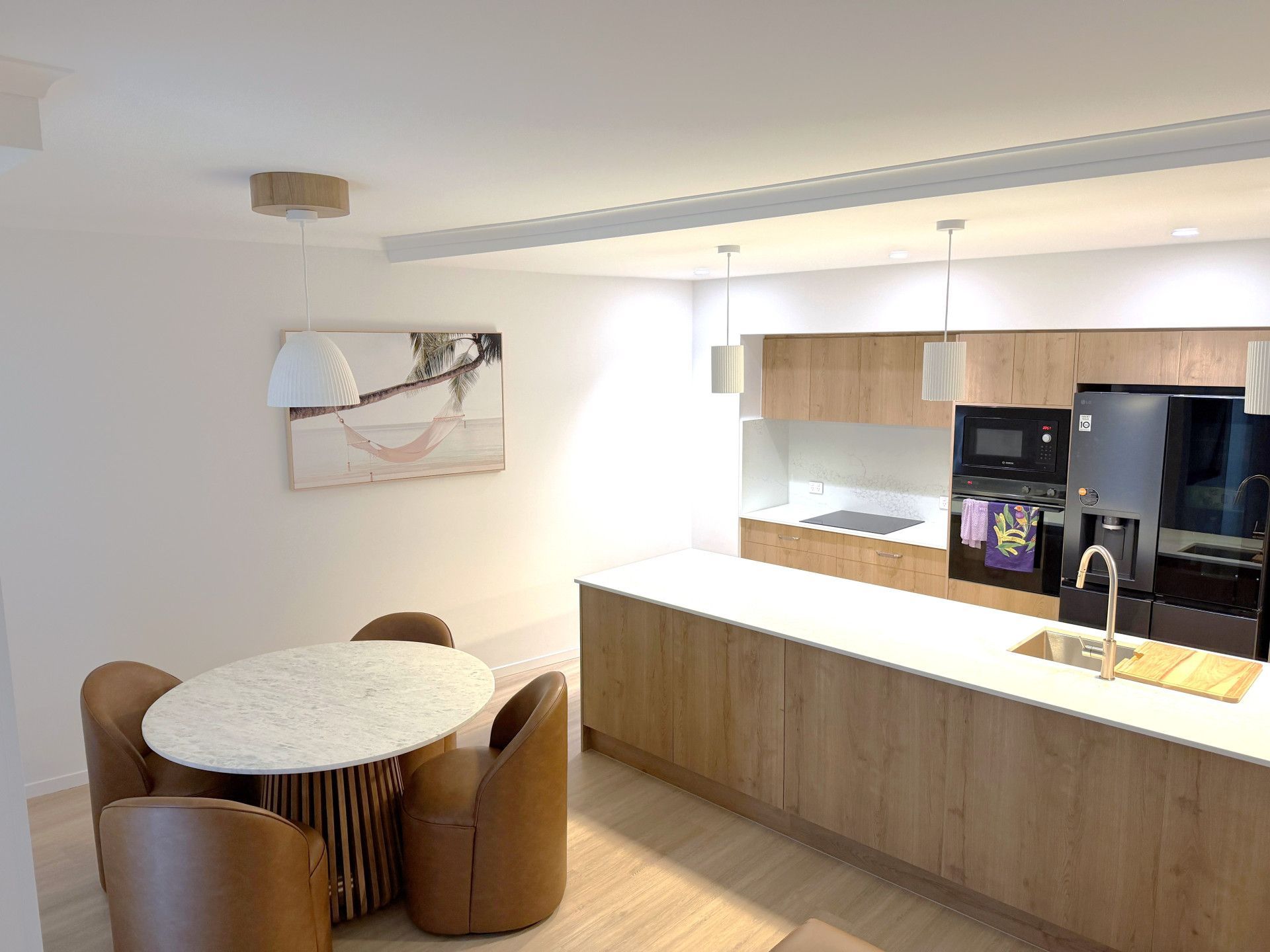 Modern kitchen with light wood cabinets, white countertops, and a dining table with brown chairs. — Nyblad Construction in Maroochydore, QLD