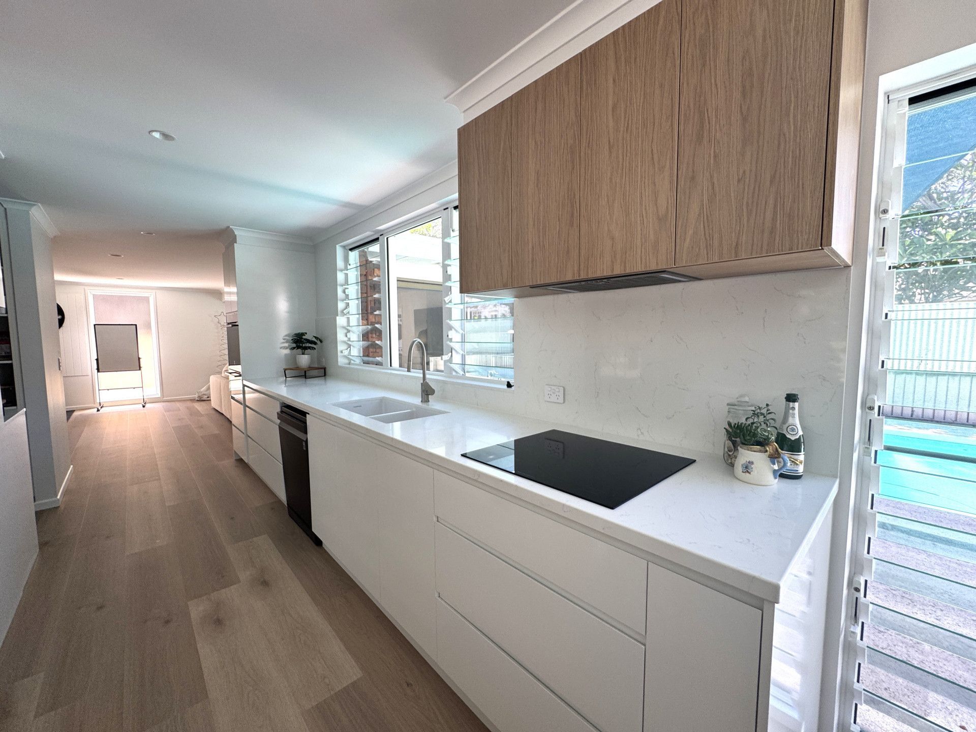 Modern kitchen with white cabinets, light wood accents, and a view of a pool.