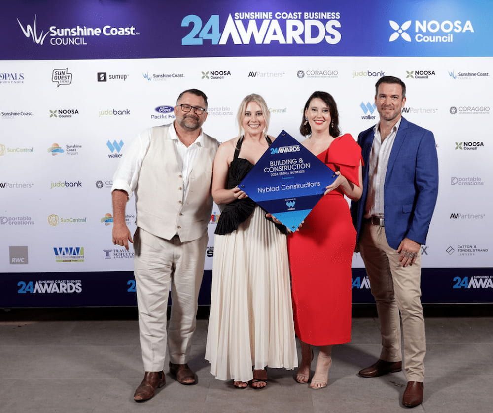 A Group of People Are Posing for a Picture in Front of a Wall — Nyblad Construction in Caloundra West, QLD