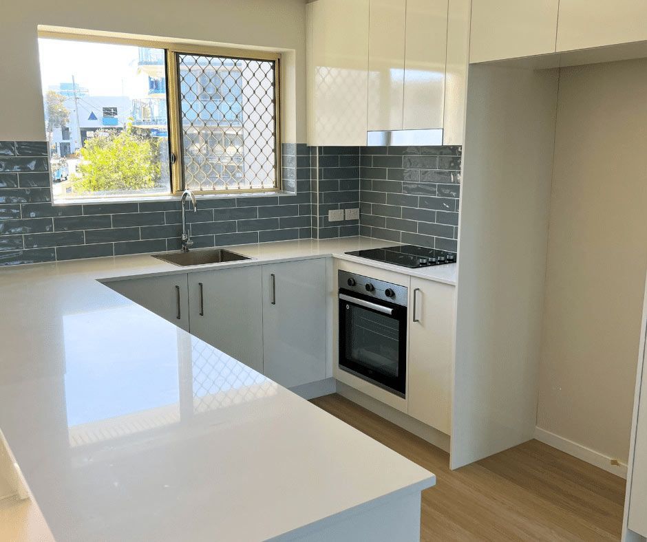 Kitchen With White Cabinets, A Stove, A Sink, And Natural Light From A Window — Nyblad Construction in Caloundra West, QLD