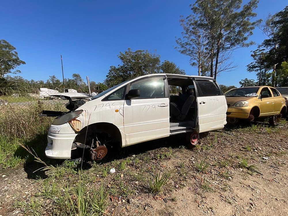 A White Van With Its Doors Open Is Parked In A Dirt Field Next To A Yellow Car — Bago Auto Dismantlers in Wauchope, NSW