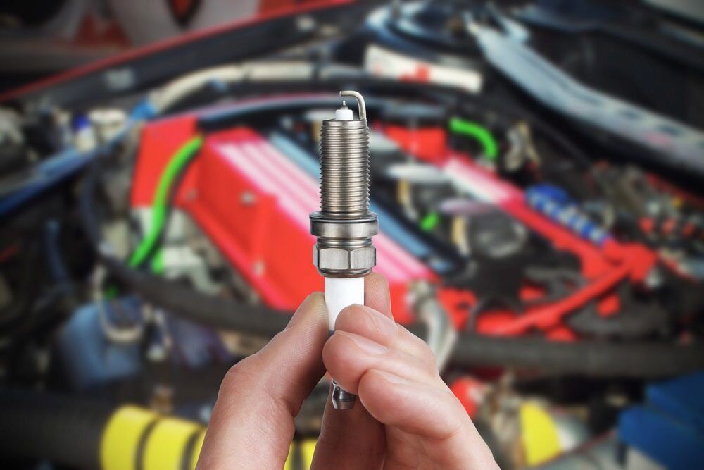 A Person is Holding a Spark Plug in Front of a Car Engine — Bago Auto Dismantlers in Taree, NSW
