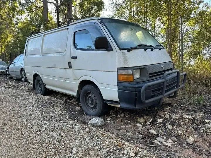 A White Van Is Parked On A Gravel Road In The Woods — Bago Auto Dismantlers in Laurieton, NSW